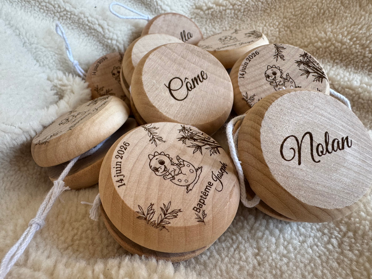 Yoyos en bois personnalisés baptême avec bébé dinosaure, prénom et date gravés sur une face, et prénoms invités gravés sur l’autre face